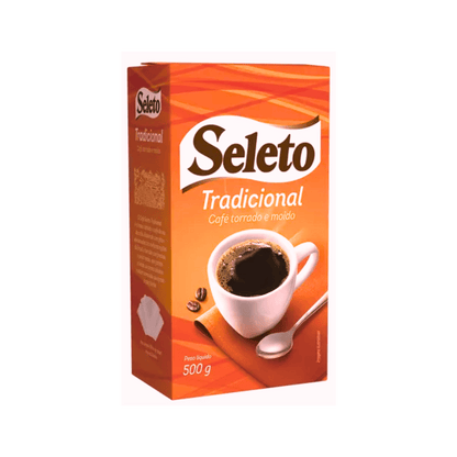 Caixa de café torrado e moído da marca Seleto, sabor Tradicional. A embalagem é predominantemente laranja e marrom, e exibe a imagem de uma xícara branca cheia de café, acompanhada por uma colher e alguns grãos. A caixa indica peso líquido de 500g.